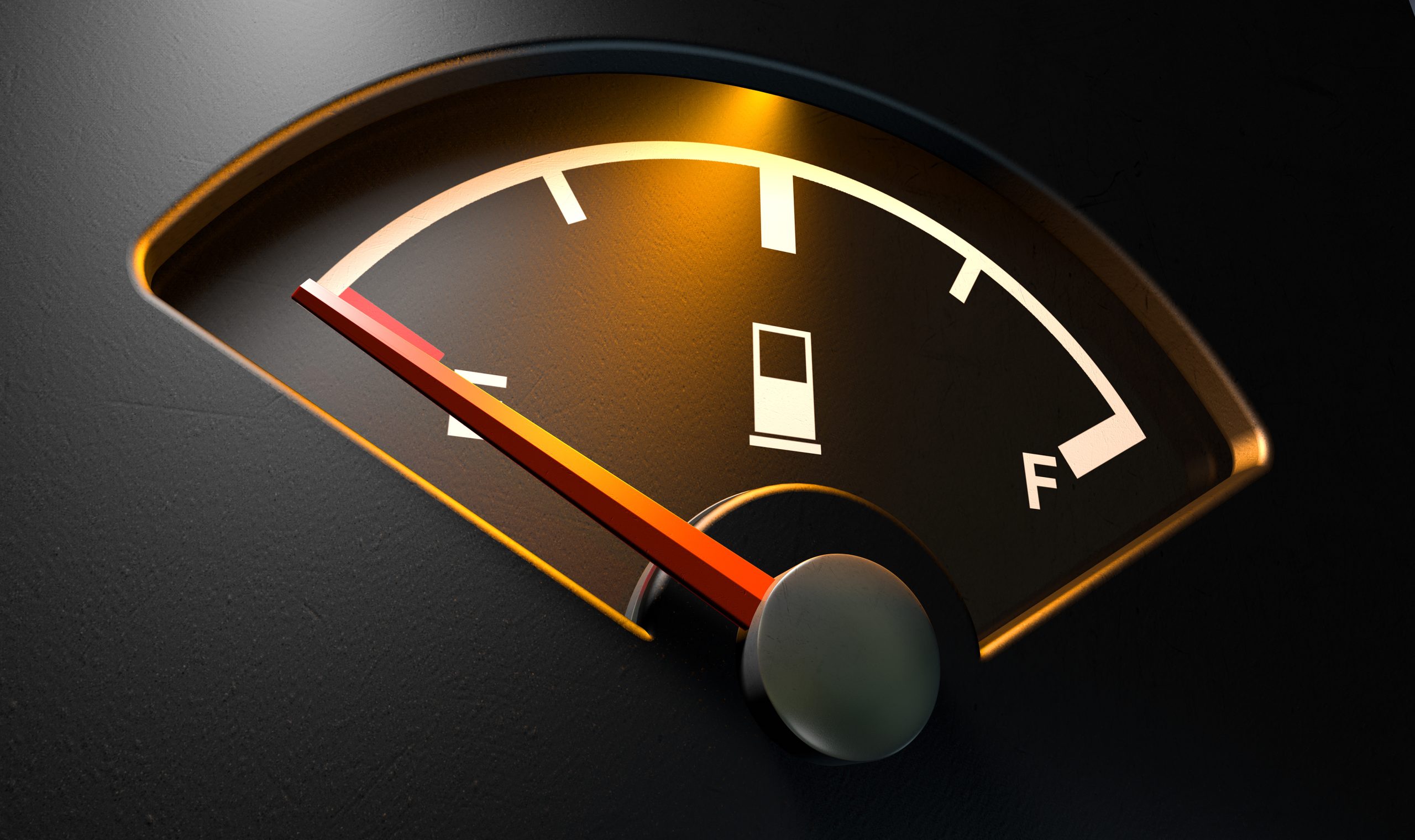 A closeup of a backlit illuminated gas gage with the needle indicating an empty tank on an isolated dark background